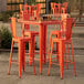 A Lancaster Table & Seating amber orange table with barstools on an outdoor patio.