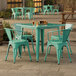 A Lancaster Table & Seating outdoor table with a teal top and four green plastic chairs.