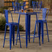 A Lancaster Table & Seating blue metal bar table with two blue bar stools on an outdoor patio.