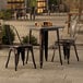 A Lancaster Table & Seating distressed copper table with two chairs on an outdoor patio.