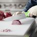 A person using a Choice 8" chef knife to slice a red onion on a cutting board.