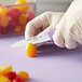 A person in gloves using a Choice serrated paring knife to cut a tomato.