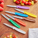 A group of Choice paring knives with different colored handles on a table with fruit.