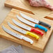 A group of Choice cimeter knives with different colored handles on a cutting board with meat and vegetables.