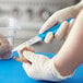 A person holding a Choice smooth edge paring knife with a blue handle to peel a piece of food.