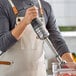 A person using a Robot Coupe MMP240VV Mini 10-inch variable speed immersion blender in a kitchen.