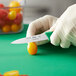 A person in gloves using a Choice serrated paring knife to cut a tomato.