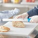 A person using a Choice serrated bread knife with a blue handle to cut bread on a cutting board.