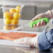 A person using a Choice 8" Narrow Semi-Stiff Fillet Knife with a neon green handle to cut a piece of salmon.