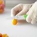 A person in gloves uses a Choice serrated paring knife with a neon green handle to cut a yellow fruit.