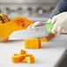 A person using a Choice 7" Santoku Knife with a neon green handle to cut a butternut squash.