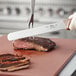 A person using a Choice bread knife to cut a piece of meat on a cutting board.