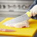 A person using a Choice 10" Chef Knife with a yellow handle to cut a chicken.