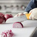 A person using a Choice neon orange Santoku knife to cut an onion.