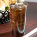 A Cambro amber plastic tumbler filled with brown liquid and ice on a table with a basket of food.