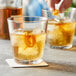 A person pouring a drink into a Pasabahce rocks glass with ice and an orange peel.