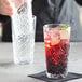 A bartender pouring a drink into a Pasabahce Timeless Vintage highball glass on a table with a glass with a drink and lime slice in it.