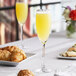 A close-up of a Nude Reserva flute glass filled with yellow liquid on a table with food and drinks.