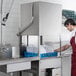 A commercial high temperature dishwasher with a rack of plates being loaded by a person in a kitchen setting.