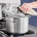 A person using a Vigor stainless steel stock pot and lid to cook on a stove.