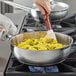 A person cooking food in a Vigor stainless steel saucier pan with a red handle.