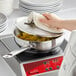 A person using a dish sponge to clean a Vigor stainless steel saucier pan on a stove.