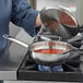 A woman cooking red sauce in a Vigor stainless steel saucier pan on a stove.