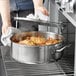 A person using a Vigor stainless steel brazier to cook chicken.