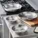 A Vigor stainless steel fry pan with aluminum-clad bottom and dual handles on a professional kitchen counter.