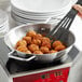 A person cooking meatballs in a Vigor stainless steel fry pan on a stove.