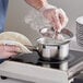 A person cooking food in a Vigor SS1 sauce pan on a stove.