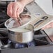 a person holding a pot with a lid over a pan on a stove