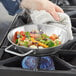 A person cooking vegetables in a Vigor stainless steel fry pan on a stove.