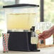 A person using a hand to pour lemonade into a Choice black beverage dispenser.