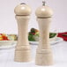 A close-up of a wooden Chef Specialties Windsor pepper mill and salt shaker on a table.