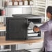 A woman in a chef's hat opening a CaterGator Dash front loading food pan carrier.