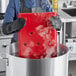 A person in a professional kitchen wearing gloves and holding a red CaterGator hot board with steam coming out of it.