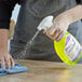 A hand using Noble Chemical Lemon Lance spray bottle to clean a table.