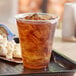 A EcoChoice PLA compostable plastic cup filled with ice tea on a plate with popcorn.