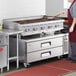 A large stainless steel gas radiant charbroiler with four control knobs, positioned on top of a two-drawer refrigerated chef base.