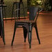 A Lancaster Table & Seating black metal arm chair with a walnut wood seat.