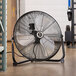 A black TPI industrial floor fan on a concrete floor.