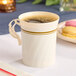 An ivory plastic coffee cup with gold accents filled with coffee.