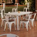 A white table with a brown edge and 6 white chairs with walnut wood seats.