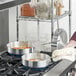 A woman in a red shirt using a Choice aluminum saute pan to cook food on a stove.
