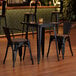 A Lancaster Table & Seating onyx black metal table and chairs with walnut wood seats in a room.