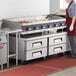 A woman in a red apron cooking on a large stainless steel countertop griddle.