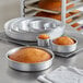 A round aluminum cake pan with a round brown cake inside.