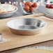 A close up of a Baker's Mark deep dish aluminum pie pan filled with a pie on a cutting board.