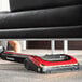 A woman uses a red and black Sanitaire TRACER cordless upright vacuum to clean under a couch in a lounge area.